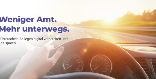 Person sitzt im Auto. Man sieht das Cockpit und schaut auf die Straße.